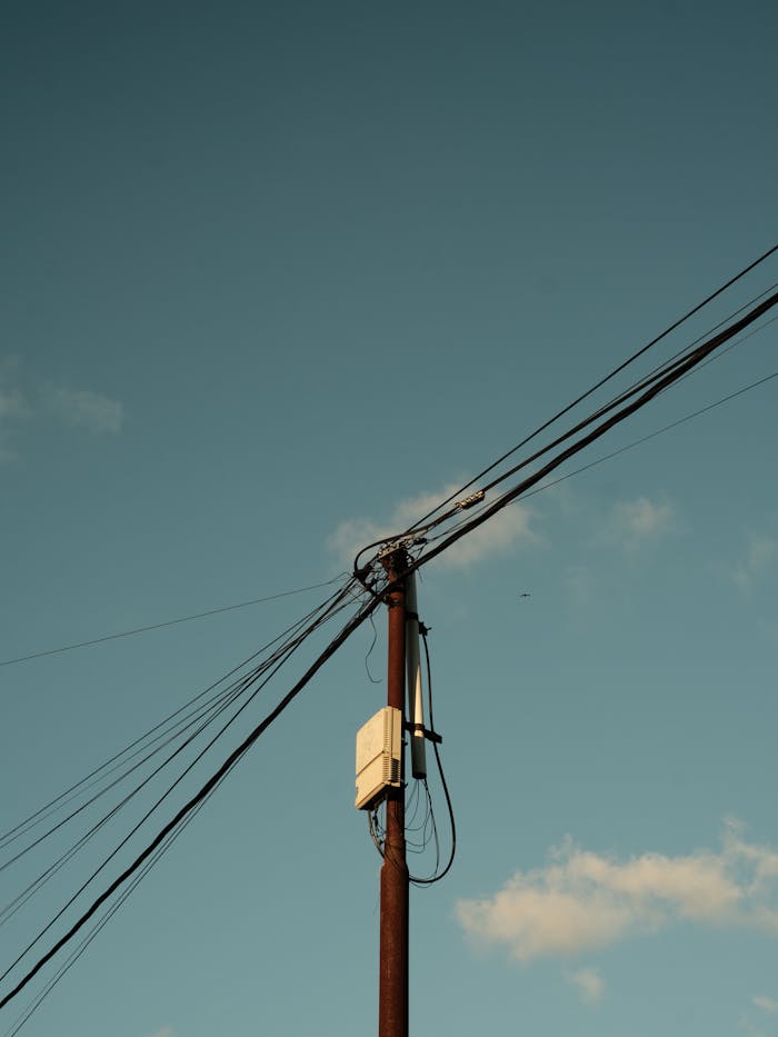 services-02 A single utility pole with power lines under a clear blue sky, signifying infrastructure and electricity.